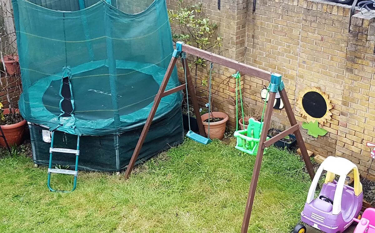 The back garden with a trampoline and safety net, swings, and a child's ride-on car.