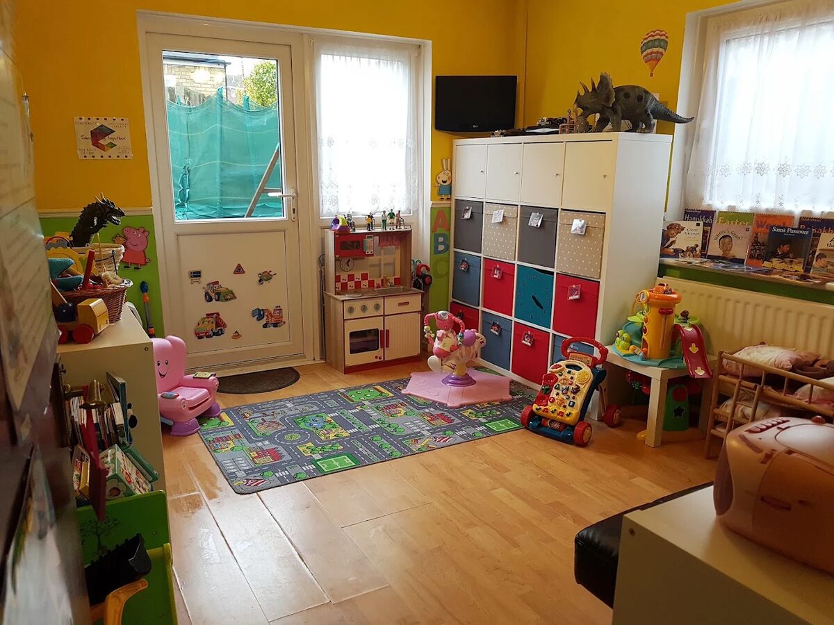The main playroom, with yellow and green walls, colourful storage, a play kitchen and toys, and the door to the garden at the back.